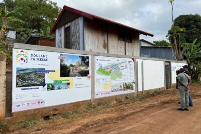 3 personnes regardant les panneaux d'information sur la façade de la maison du projet de la ZAC de Doujani. - Agrandir l'image 6 sur 8, fenêtre modale