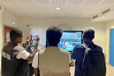 Journalistes de dos regardant la vidéo promotionnelle de la 3ème édition de la course de pirogues de Mamoudzou - Agrandir l'image 3 sur 5, fenêtre modale