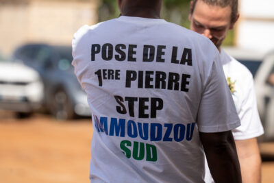 Personne de dos portant un t-shirt avec les inscriptions "Pose de la 1ère pierre STEP Mamoudzou sud" - Agrandir l'image 3 sur 3, fenêtre modale
